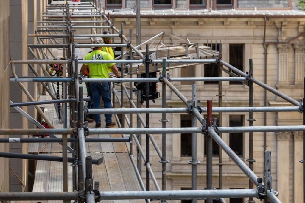 Two men standing on a scaffold, wearing safety helmets and harnesses