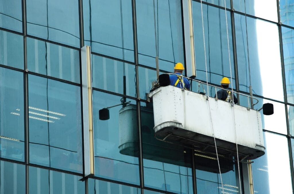 Two men in uniforms cleaning a large glass door in a commercial space