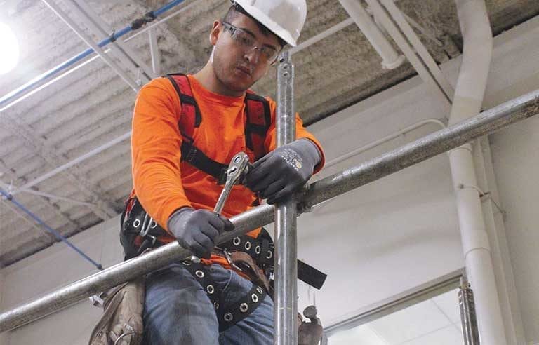 A scaffolder working on a construction site, adjusting and fixing a metal pipe while standing on scaffolding