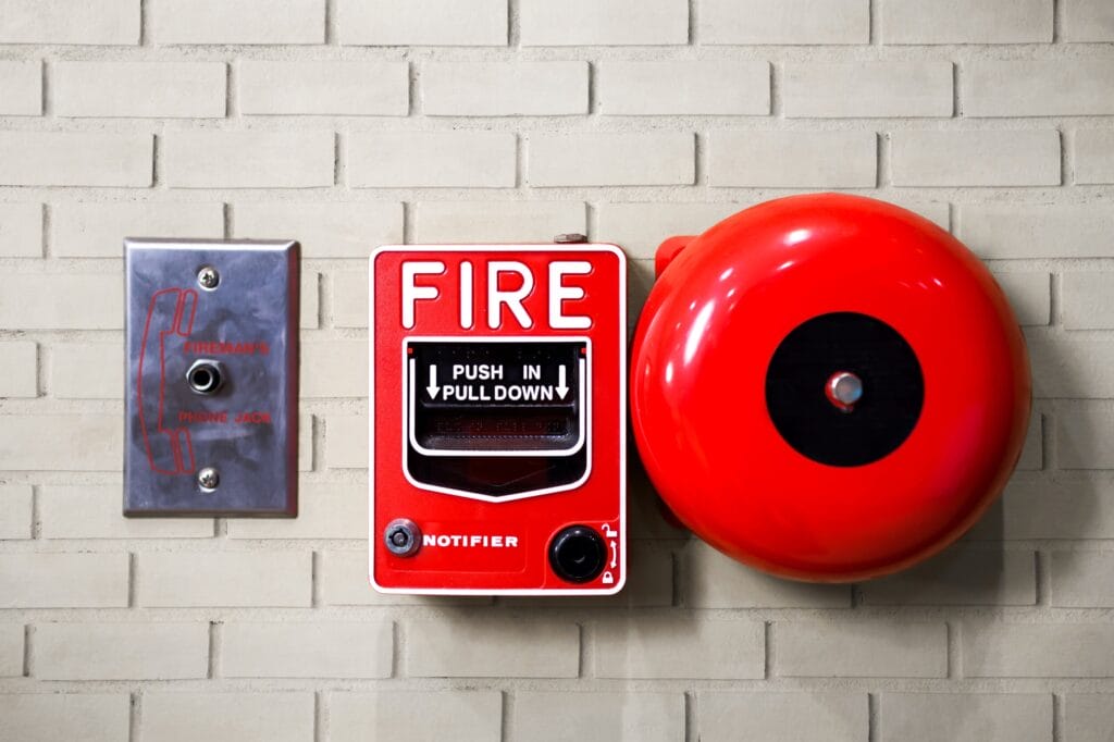 image shows a fire alarm pull station with a bell mounted on a tiled wall