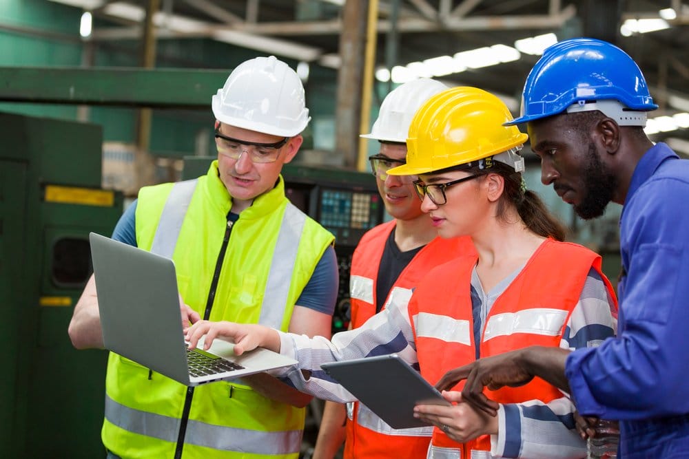 Construction workers engaged in a discussion on-site, with one pointing to plans or materials while the others listen and respond