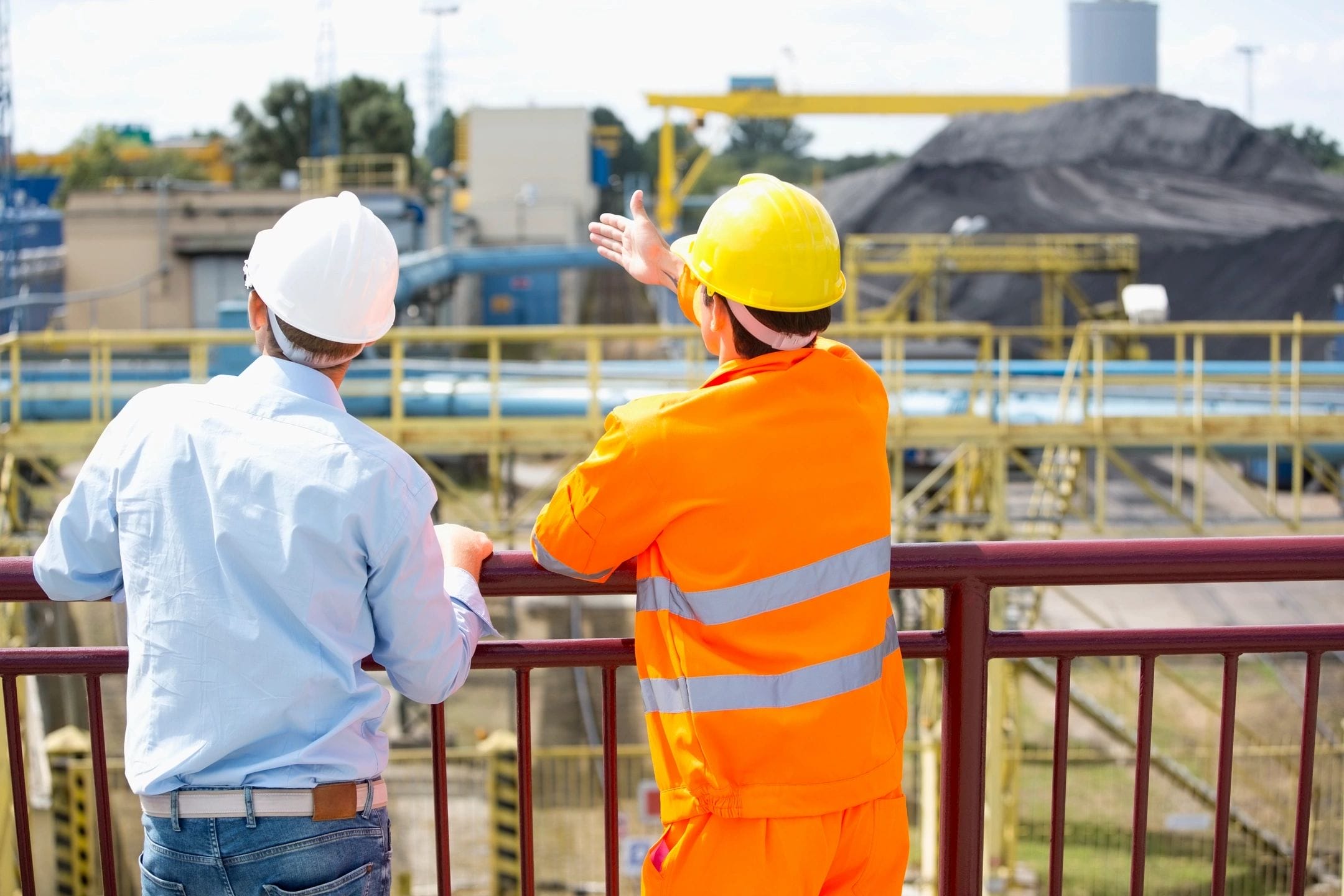 Two workers engaged in a discussion on-site, with one pointing to something and the other listening attentively, both wearing work attire and safety gear