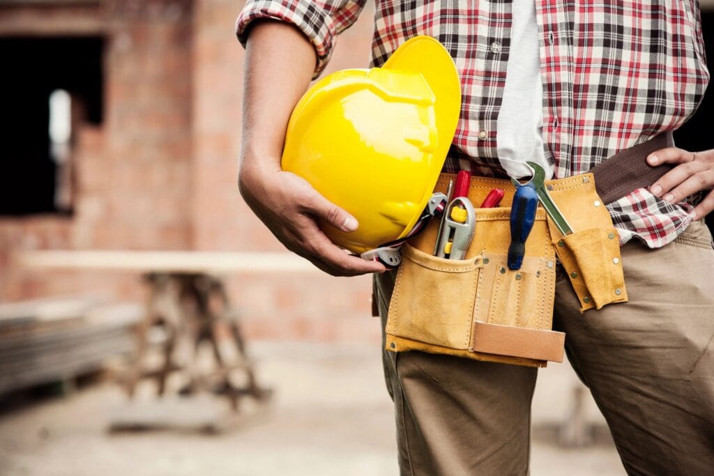 A construction worker holding safety helmets in one hand, while wearing their own safety gear and standing on a construction site