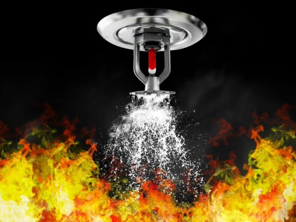 The image depicts a fire sprinkler in action, spraying water onto a fire.