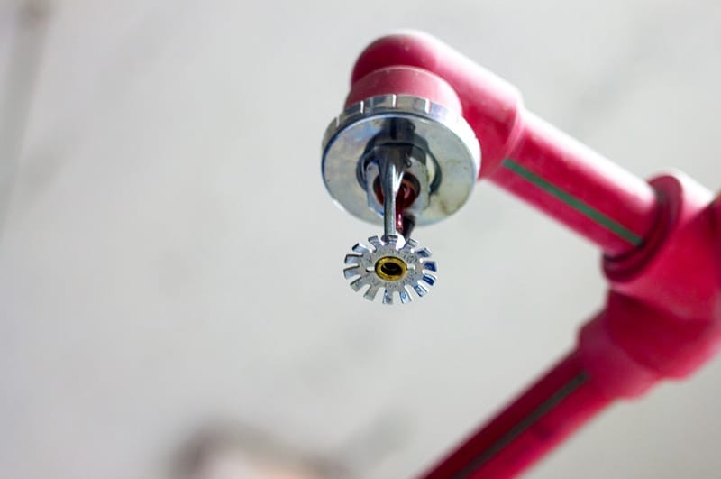 The image shows a fire sprinkler head attached to a red pipe.