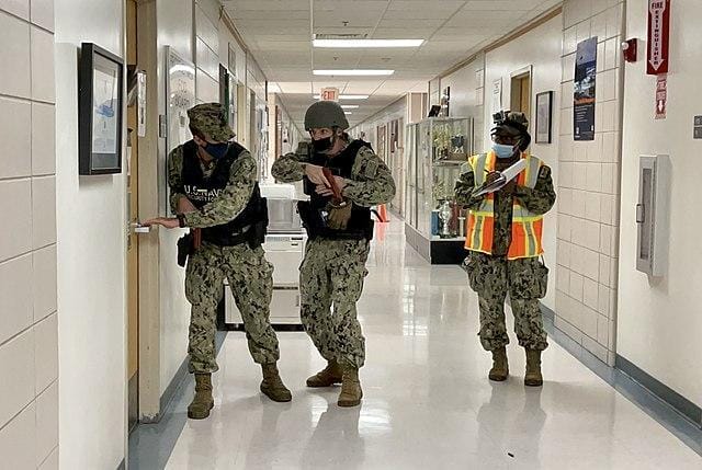 The image shows three armed soldiers in a hallway, possibly conducting a training exercise